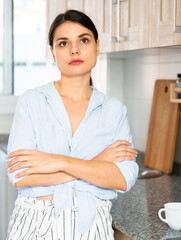 Portrait of upset tired young woman standing at home kitchen table