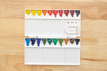 Colorful watercolor paints set in watercolor palette on wood.