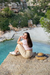 Fototapeta na wymiar Woman sitting on a cliff overlooking a summer beach. Relaxing moment, summer, refreshing.