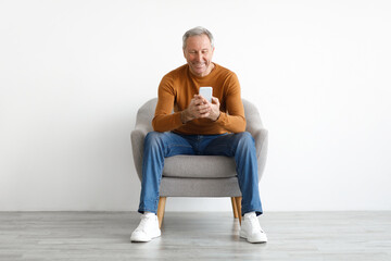 Portrait of smiling mature man using smartphone sitting on chair