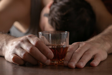 Alcoholism, alcohol addiction and people concept - male alcoholic with glass of whiskey lying or sleeping on table