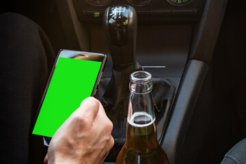Man drinking alcohol while driving in his car and looks in smartphone - obrazy, fototapety, plakaty