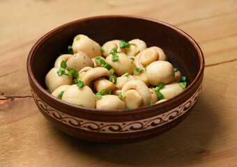 mushrooms with green onions in a clay plate, pickled champignons, one object on a wooden background
