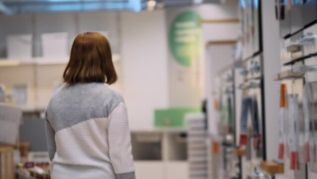 A woman in casual clothes and a mask on her face walks through a furniture store slowmotion defocused