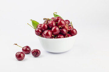 Ripe sweet cherries in a white bowl on white background.