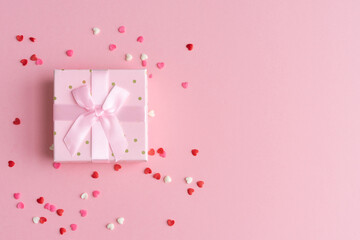Gift box with ribbon bow and topins decoration on pink background. Copy space.