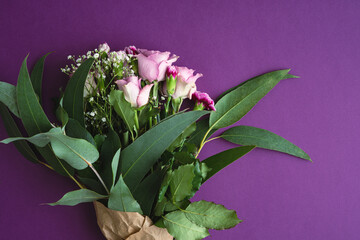 Bouquet with purple roses and eucalyptus on purple background. Copy space. Top view.