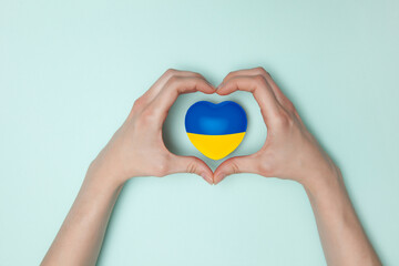 Heart with print the national flag of ukraine in female hands on light blue background. Flat lay....