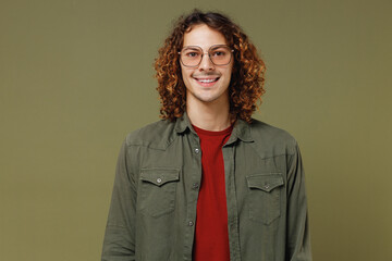 Smiling cheerful happy fascinating jubilant fun long curly hair young brunet man 20s years old wears khaki shirt jacket glasses looking camera isolated on plain olive green background studio portrait.