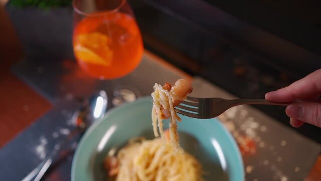 person eats italian carbonara pasta with seafood, shrimps, aperol spritz glass