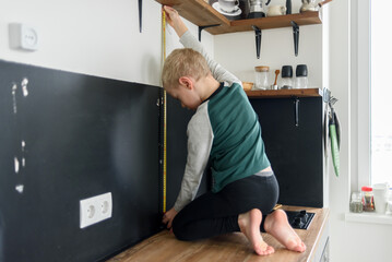 Boy child using metal tape measure to renovation works at home kitchen