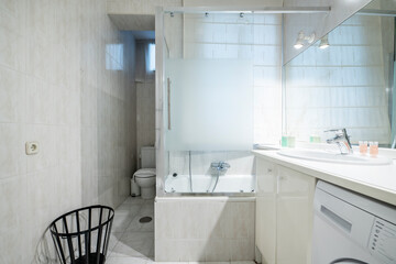 White porcelain sink on a round resin countertop next to an opaque glass shower stall with a white washing machine below and a toilet in the background