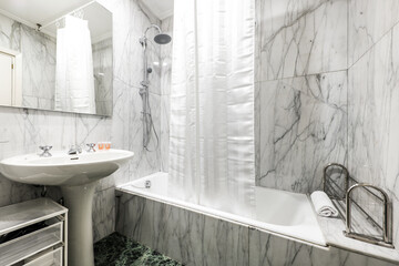 Bathroom with white tub, earthenware sink and square mirror with frame and marble floors