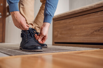 A man standing and tying shoelaces at home in hall.