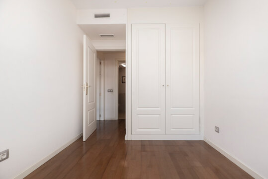 Room with dark parquet floors, fitted wardrobes with white lacquered wooden doors and air conditioning through internal ducts.