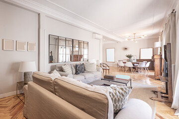 Living room with large sofas, wall covered with square mirrors, square coffee tables, wooden floors, plaster moldings on the ceilings and pastel paint