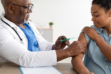 Black Woman Receiving Vaccine Injection Sitting With Doctor Indoor