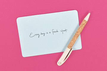 Motivational text 'Every day is a fresh starts' on blue paper note on pink background
