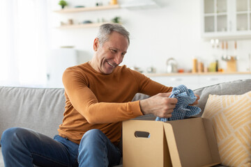 Happy mature man unpacking parcel after online shopping