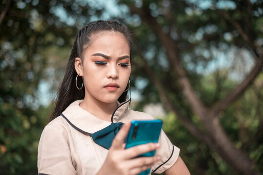 A young asian student is displeased after receiving a message or reply filled with obscenities or profanities on her phone. Dealing with a troll or basher on her social media.