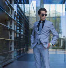 three quarter lenght shot of a handsome man in formal suit with a rogue expression in his shaved face while standing with hands in pockets in an entry of an offices building