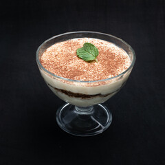 Traditional Italian home made tiramisu dessert in a glass cup on a black  background