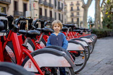 Child, standing next to a row of red bicycles for public transportation in Barcelona