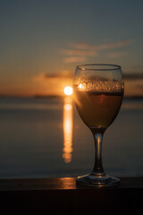 A glass of white wine at sunset, by the sea. Sandy beach, summer, warm evening.