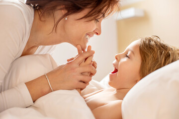 Mother and child, blond toddler boy, cuddling in bed in the morning, love and tenderness