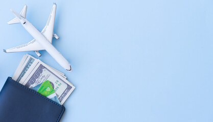 Blue wallet with money and a bank card, next to a figurine of an airplane