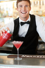 Quenching any ladys thirst. Young handsome barman laughing and smiling while wipping up a delicous and tasty cocktail.