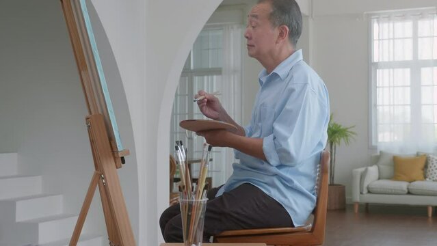 Older Asian men are happy together painting with watercolors on vacation at home, happy and laughing. Concentrate on drawing and appreciating your own work, the concept of creating art.
