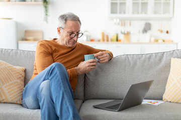 Mature man watching video on computer, drinking coffee