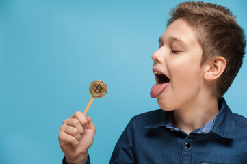 The boy sucks and licks a bitcoin lollipop. The concept of mining or earnings