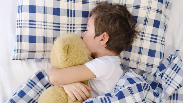 little kid boy sleeping in bed with toy. Cute healthy little toddler baby boy child sleeping. taking a nap under blanket in bed while hugging teddy bear
