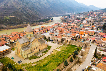 Fototapeta na wymiar View from drone of ancient Orthodox Svetitskhoveli Cathedral against background of spring cityscape of Mtskheta in valley of Caucasus mountains in Georgia