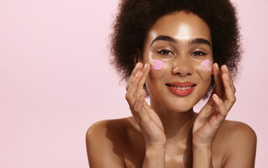 Vertical shot of beautiful african american girl with curly hair, using face mask on cheek,...
