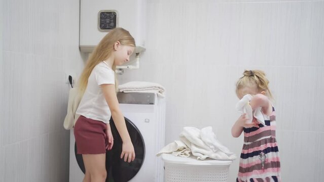 two cute and cheerful girls play with laundry in the laundry room. 