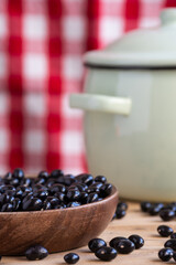 Close-up of small black beans (caricos) in wooden bowl and green pot on rustic table, selective focus, red background, vertical