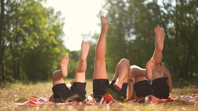 kid playing in the park. a group of children lie on their backs swinging their legs. happy family kid dream concept fun. happy family kids raised their feet up on nature in the park