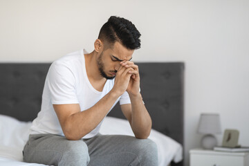 Fototapeta premium Portrait Of Sad Pensive Middle Eastern Man Sitting On Bed At Home