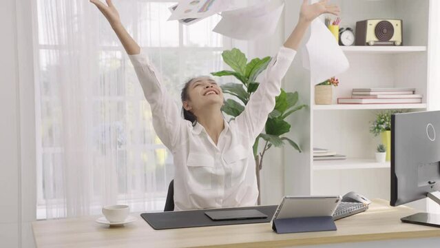 Slow motion Freelance Asian woman rejoices after online meeting via tablet when project is done and very successful by throwing up the paperwork and doing a hand that shows success.