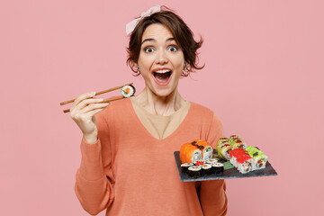 Young excited woman in casual clothes hold in hand makizushi sushi roll served on black plate...