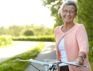 She enjoys healthy outdoor activities - Cycling. Smiling senior woman standing on a country lane...