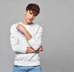 Young handome man in white sweatshirt over gray background