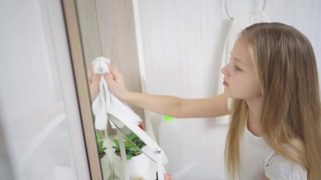 a cute little girl washes sink and the bathroom mirror with a special cleaner.