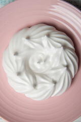 One large meringue on a pink saucer. Home confectionery flatley. Old retro white and blue table.