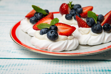 Four cakes Anna Pavlova with blueberries and strawberries with a mint leaf on a beautiful plate....