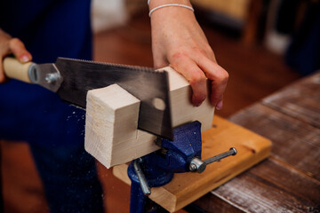 Close-up of a woman's hands sawing a wooden bar. Handmade wood products.