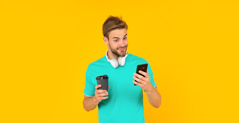 amazed man hold smartphone and coffee cup on yellow background, communication